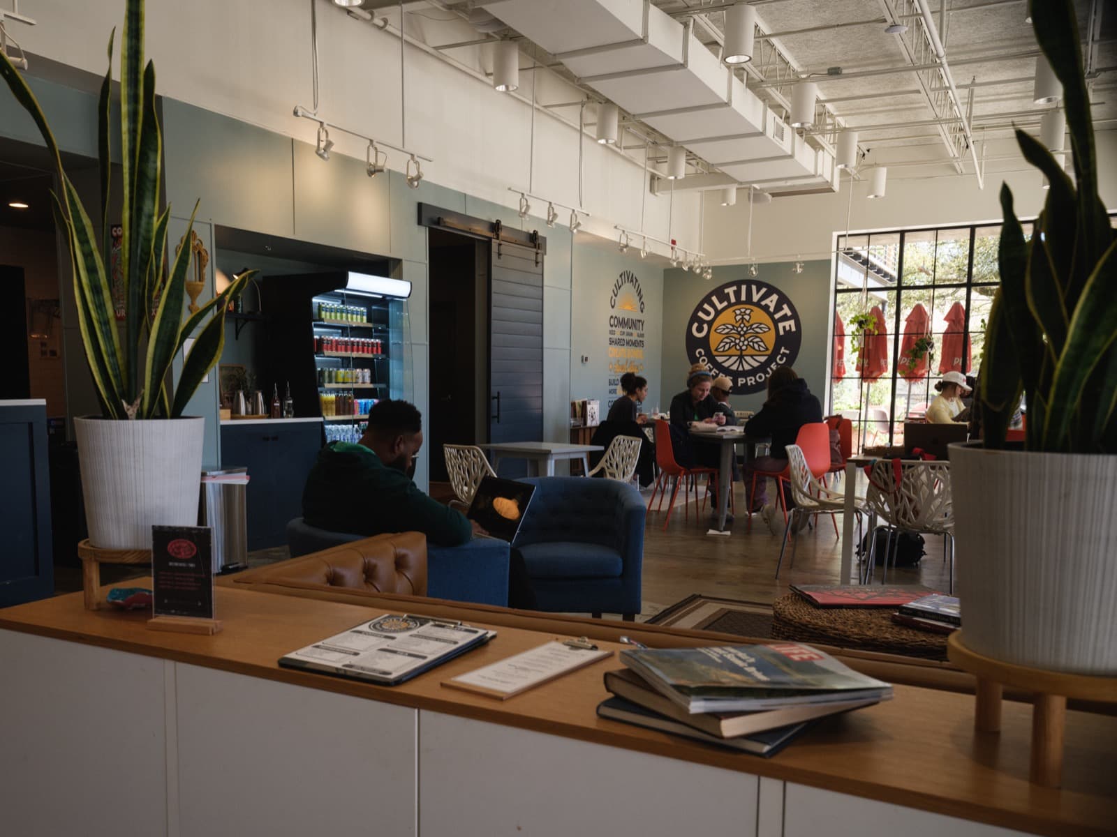 Cultivate Coffee Project interior with lounge seating, logo wall mural, and guests